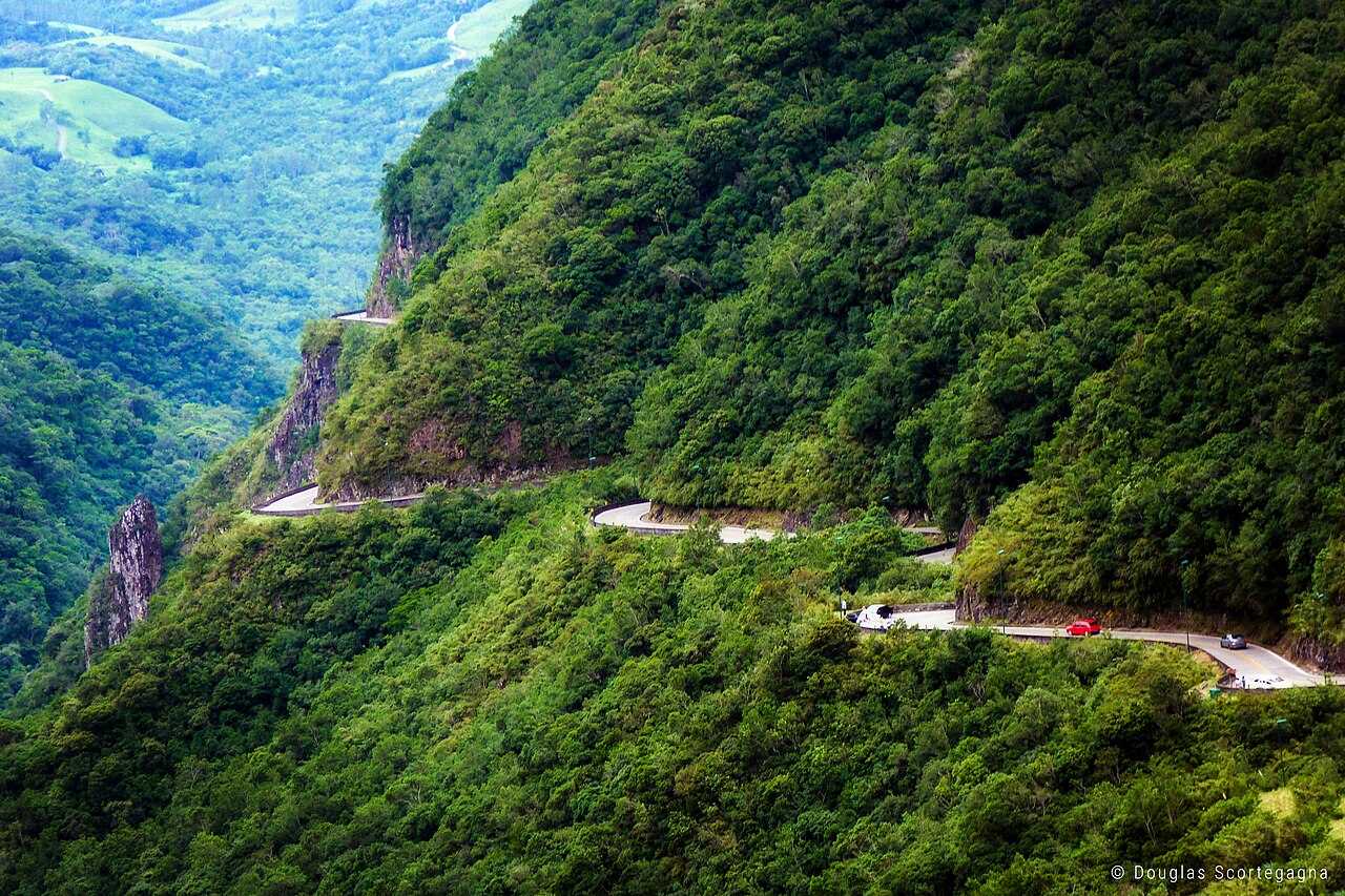 Estrada sinuosa descendo uma serra coberta de mata